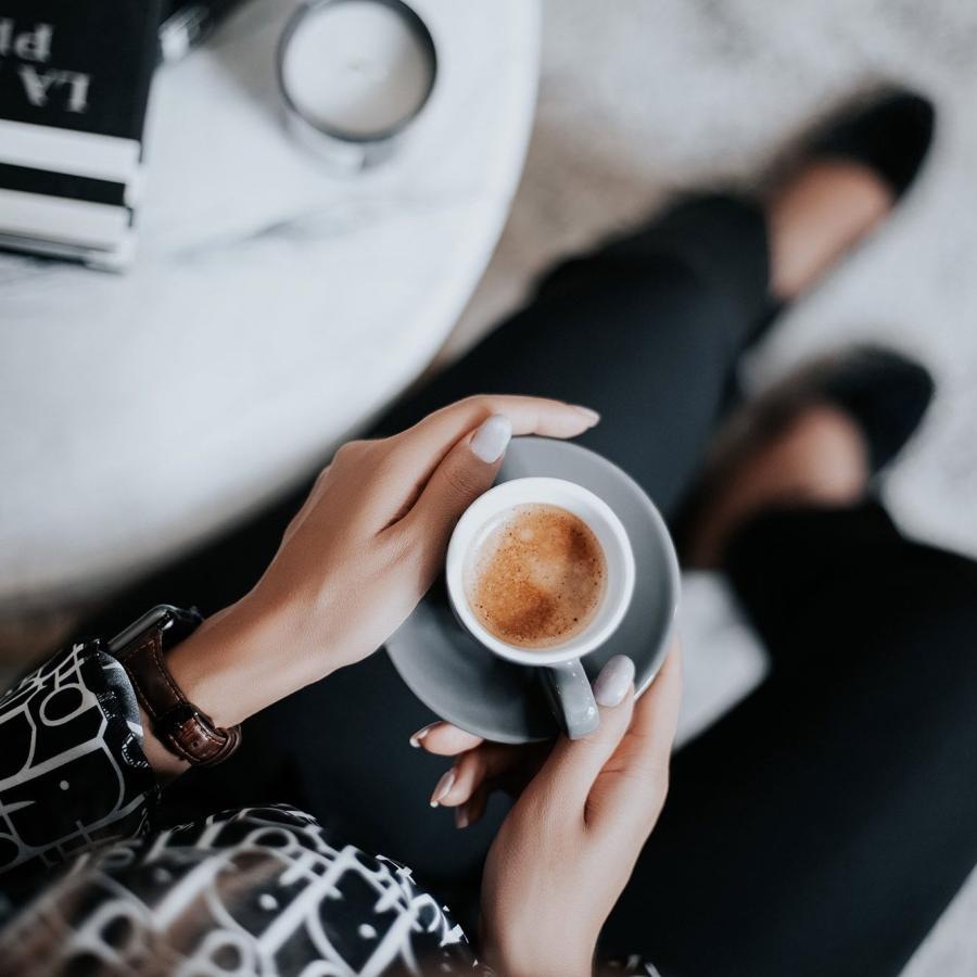business woman sits next to a marble table with books and holds a saucer with a cup of espresso